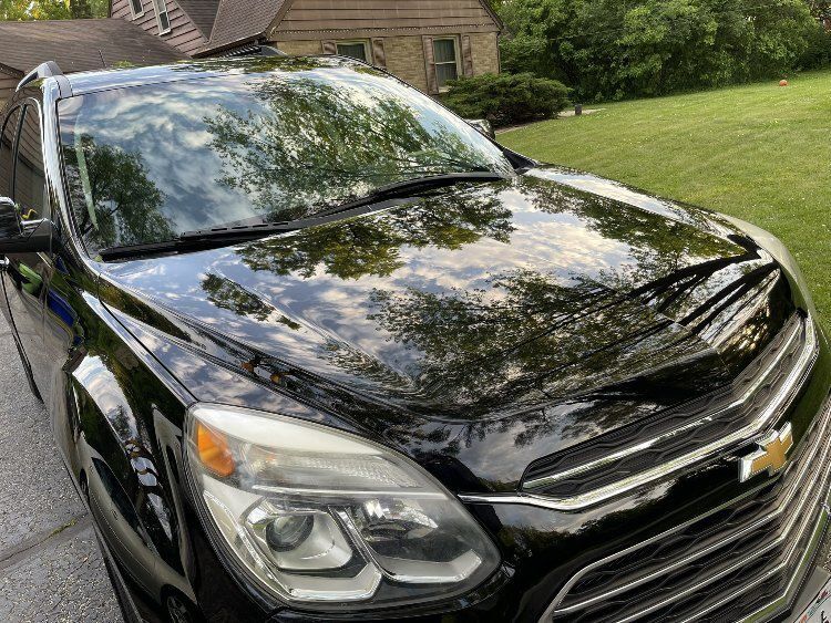 Black Chevrolet SUV with a glossy finish reflecting trees and sky, showcasing professional detailing service by On Demand Detailing.