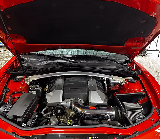 Engine compartment of a red luxury car showcasing detailed components, including polished engine parts and a clean interior, emphasizing professional vehicle care and maintenance.