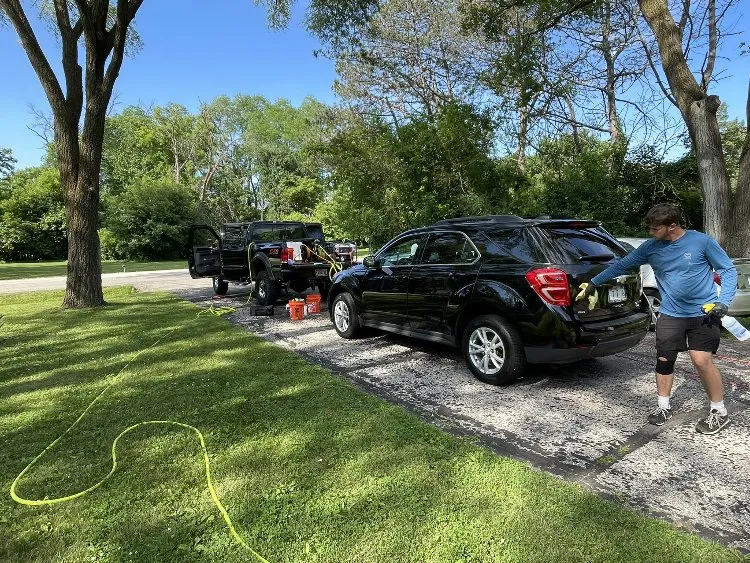 Man detailing a black SUV on a driveway with a mobile detailing setup